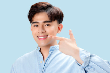 Happy young Asian smart man pointing finger to whitening teeth  over isolated blue background.