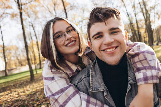 Heterosexual caucasian young loving couple walking outside make selfie in sunny weather, hugging smiling kissing laughing spending time together. Autumn, fall season, orange yellow red maple leaves