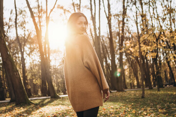 Attractive pretty woman walking outdoor, portrait of young lady in warm sunny autumn park season, fall, yellow orange red leaves, dressed wool sweater smiling having fun 

