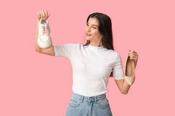 Young woman with shoe and sneaker on pink background. Feminism concept