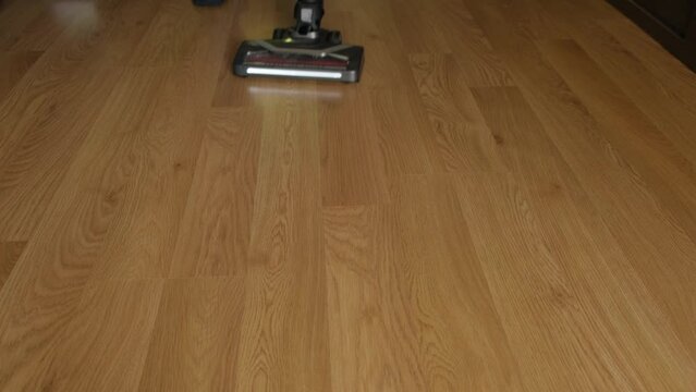 A cordless vacuum cleaner with a turbo brush and lighting cleans a laminate floor close-up.