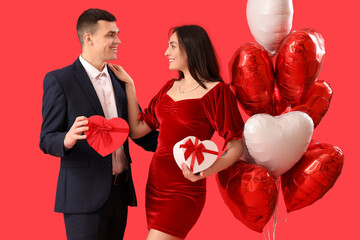 Young couple with gifts and heart-shaped balloons on red background. Valentine's Day celebration