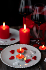 Obraz na płótnie Canvas Saint Valentine's Day celebration. Red burning candles, hearts, gift box, postcard on dark wooden background. Happy holiday . Table decor for festive dinner, romantic atmosphere