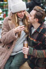 Winter romance. Happy young couple I warm clothes enjoying outdoor christmas market, having fun. Drinking hot chocolate, tea or mulled with from thermos. Cozy holiday atmosphere, festive mood