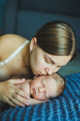 A newborn baby with his mother lies on a gray soft blanket. A mother hugs her newborn baby.