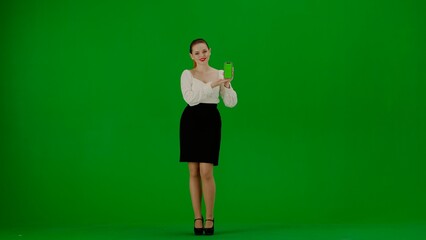 Portrait of attractive office girl on chroma key green screen. Woman in skirt holding mobile phone with mockup and talking at camera, advertises service