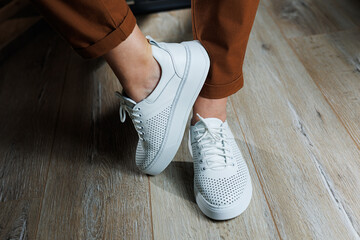 Close-up of female legs in white perforated leather sneakers. Women's summer sneakers. Collection...