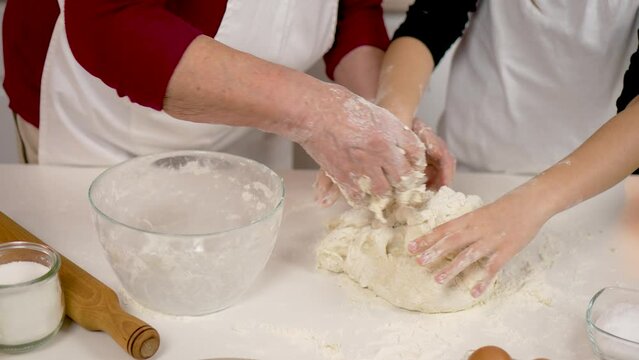Close up hands kneading dough. Mature woman wears apron engaged in homemade baking with little girl recipes for making fragrant bread in kitchen. Grandmother enjoy process of cooking pie with