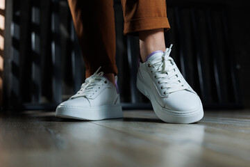 Comfortable women's sneakers on a flat sole with laces. Close-up of female legs in white perforated leather sneakers. Women's summer sneakers. Collection of women's leather shoes