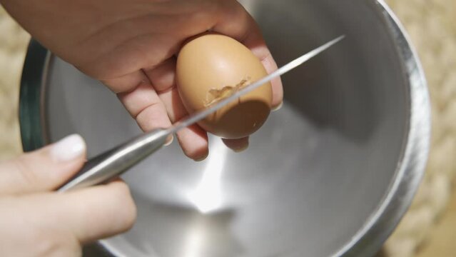 Chef breaks chicken farm fresh eggs into a silver bowl.