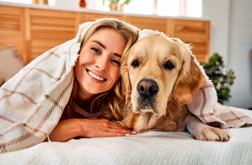 Similarity between dog and owner. Portrait of cheerful woman with blond hair snuggling to adorable...