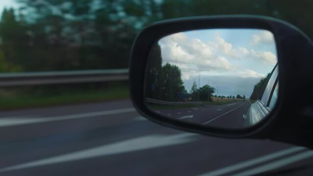 Car journey under varied skies: Sunny and cloudy horizon view in backside view mirror