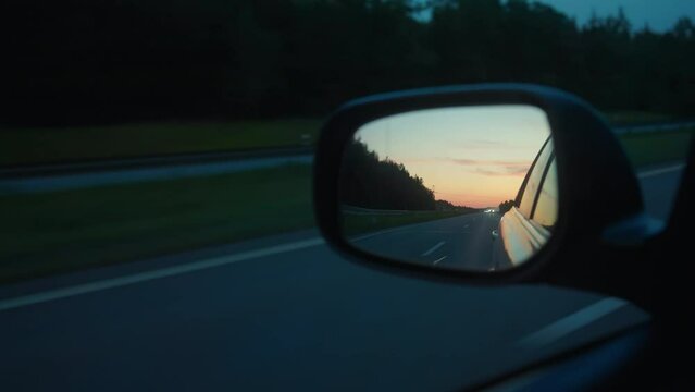 On the road beneath a changing evening sky through side mirror: Driving towards sun and clouds