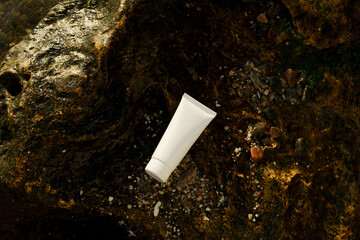 White mockup of a tube of moisturizer or sunscreen for facial skin on a wet stone near the sea. Concept of natural cosmetics, beauty products