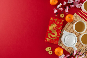 Obraz na płótnie Canvas Honoring tradition: chinese New Year tea ceremony. Top view photo of teapot, cups of tea, tangerines, money envelope, traditional decorative elements on red background with advert area