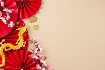 Arranging an exquisite Chinese New Year décor arrangement. Top view shot of red folding fans, sakura, gold dragon, lanterns, gold coins, on beige background with advert spot