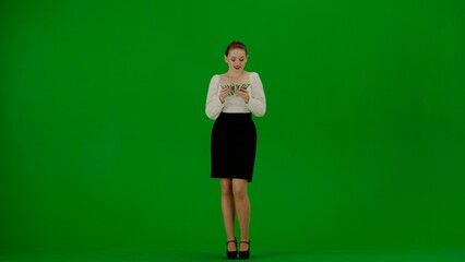 Fototapeta na wymiar Portrait of attractive office girl on chroma key green screen. Woman in skirt and blouse standing counting money, happy smiling face expression.