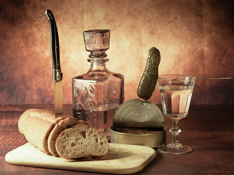 Antique-style still life with alcohol, vodka, canned fish, bread and cucumber.