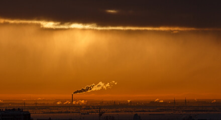 Plumes of factory smoke rise from the chimneys into the sky at sunset. The chimney emits exhaust...