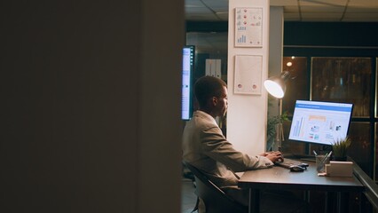 Revealing shot of employees checking company figures, postings and documents for accuracy during nighshift. Staff member working overnight, analyzing stored computerized financial information