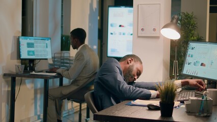 Drowsy accountant sleeping in office, being woken up by colleague shocking him. Worker scaring unsuspecting tired coworker, shaking him up in his desk chair during nightshift