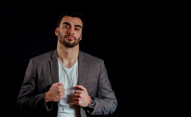 Handsome macho man with beard posing in jacket and white shirt on black background  