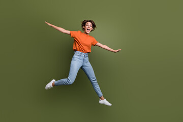 Fototapeta na wymiar Full size photo of funky woman dressed orange t-shirt jeans in glasses flying hold arms like wings isolated on khaki color background