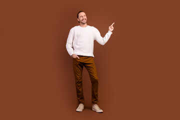 Fototapeta na wymiar Full length photo of dreamy charming man wear white sweater showing finger looking empty space isolated brown color background