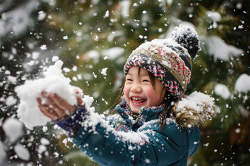 Happy kid wearing warm clothes plays outdoors with snow in winter.