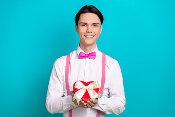 Photo portrait of handsome young guy hold heart gift box ribbon wear trendy pink garment isolated on cyan color background