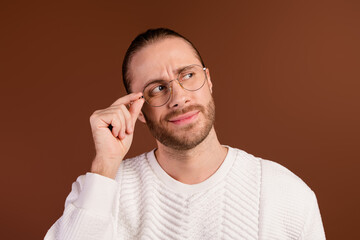 Photo of smart suspicious man wear white sweater arm hand spectacles looking empty space isolated brown color background