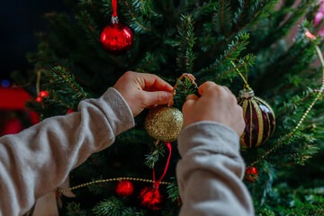 close up on child hands holding christmas tree decoration putting it on tree