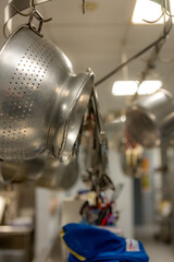 Stainless steel pots and pans and other cooking utensils hanging in a commercial industrial kitchen. 