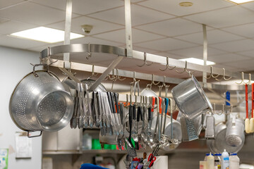 Stainless steel pots and pans and other cooking utensils hanging in a commercial industrial...