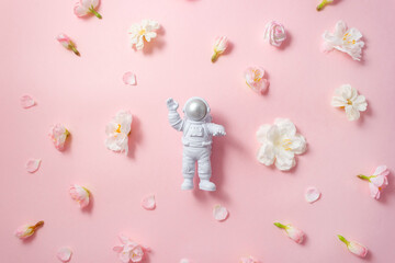 Astronaut is surrounded by decorative flowers on pink background. Holiday banner. Selective focus.