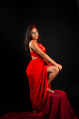 Fototapeta premium Beautiful young woman dressed in red with her foot on a chair posing for the photo.