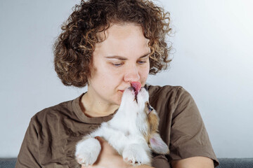 Love and tenderness. Portrait of attractive brown-haired woman, holding funny fluffy velshkorgi puppy in her hands.