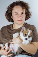 Portrait of young attractive brown-haired woman in T-shirt, holding funny fluffy velshkorgi puppy in her hands,.