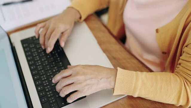Asian senior woman types text working with laptop computer 