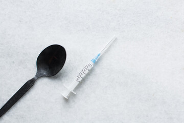 Overhead view of a syringe, black spoon, powder and rope, tools for using cocaine and heroin on a white table, concept photo of drug use - obrazy, fototapety, plakaty