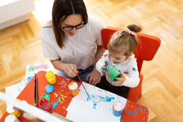 Fototapeta premium The little girl and her mother enjoy painting, they are all dirty but happy