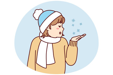 Little teen girl stretches out palm to pick up snowflakes standing outdoors in cold weather. Child in hat and scarf enjoys winter holidays and looks with surprise at falling snow. Flat vector image