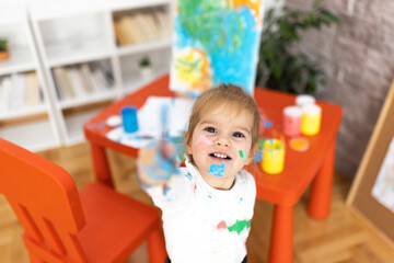 The little girl enjoys painting, she is all dirty but happy