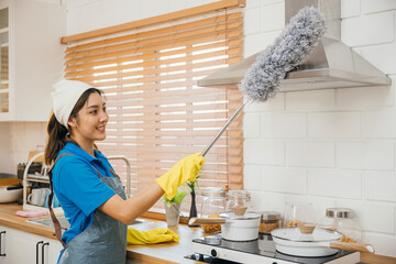 Asia woman in maid workwear gloves and apron cleans home dusts kitchen ventilation. Emphasizing housework modern hygiene equipment. Clean air whisk portrait. maid housekeeping concept. - obrazy, fototapety, plakaty