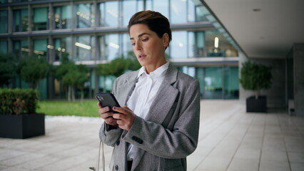 Annoyed businesswoman text phone at office center. Nervous executive send reply