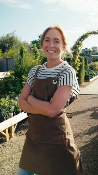 Vertical video portrait of smiling woman wearing apron working outdoors in garden centre - shot in slow motion