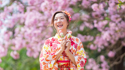 Japanese woman in traditional kimono dress holding sweet hanami dango dessert while walking in the...