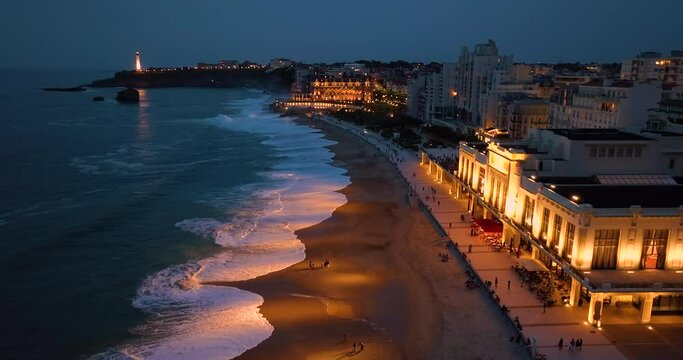 Aerial view incredibly beautiful view of the city of Biarritz at night. Ocean waves illuminated by night lights wash the beaches of the night tourist city. France