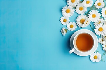 Flat lay image of chamomile tea in a white cup, with daisy flowers and dry tea on a blue background.