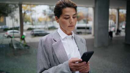 Serious businesswoman messaging smartphone on street. Focused woman typing cell